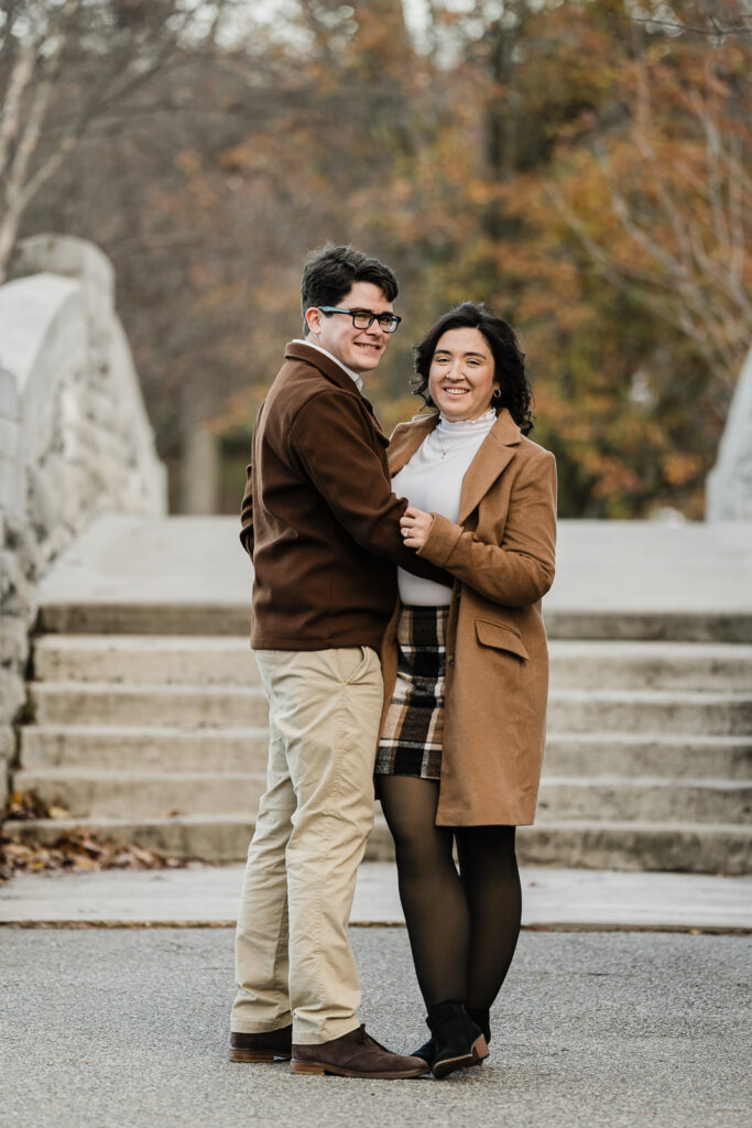 Engaged couple standing together with fall foliage background at Verona Park photographed by Alex Kaplan
