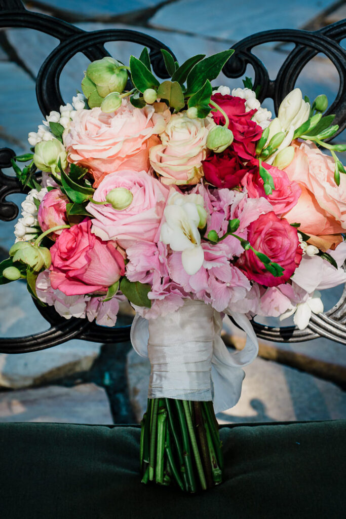 Detailed shot of wedding bouquet with pink roses, ranunculus, and greenery on ornate iron chair