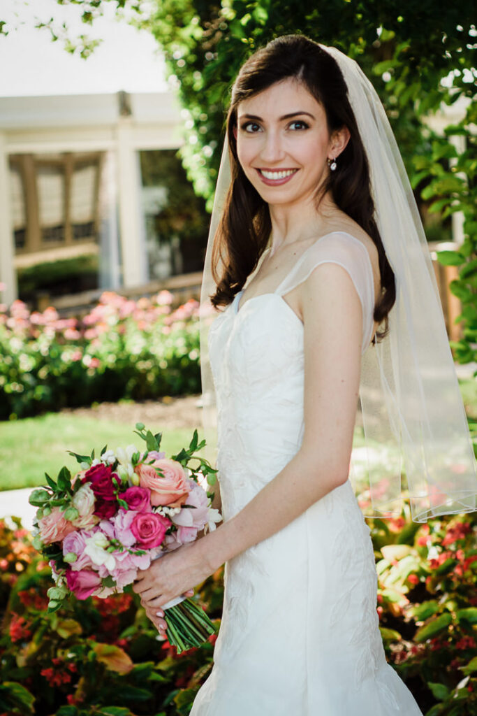 Bride holding colorful bouquet in fitted wedding dress with begonia gardens in background