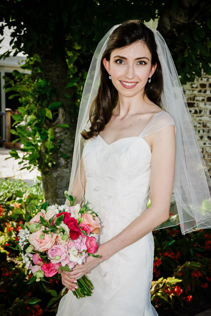 Beautiful bride with flowing veil and romantic bouquet smiling in outdoor garden setting