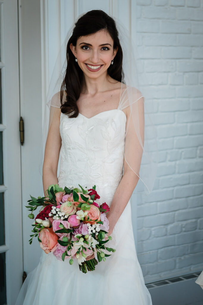 Radiant bride in fitted wedding dress with veil holding pink and crimson bouquet at Hamilton Farm Golf Club