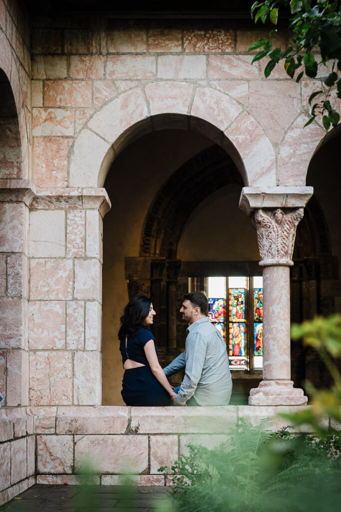 Couple holding hands in medieval stone archway with colorful stained glass windows at The Cloisters