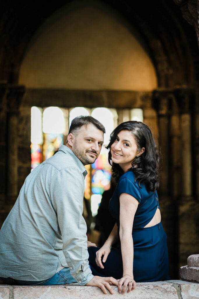 Engagement portrait of couple sitting with stained glass and medieval architecture at The Cloisters NYC