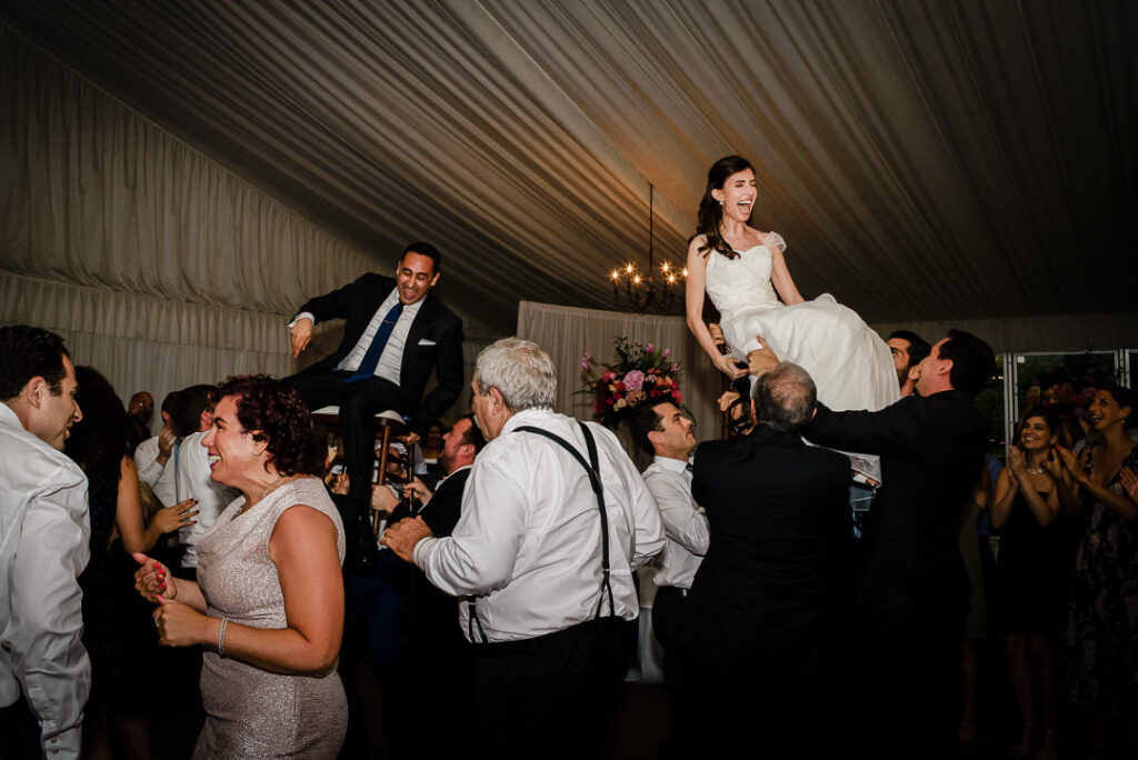 Bride and groom both lifted on chairs by family and friends during traditional Jewish Hora dance