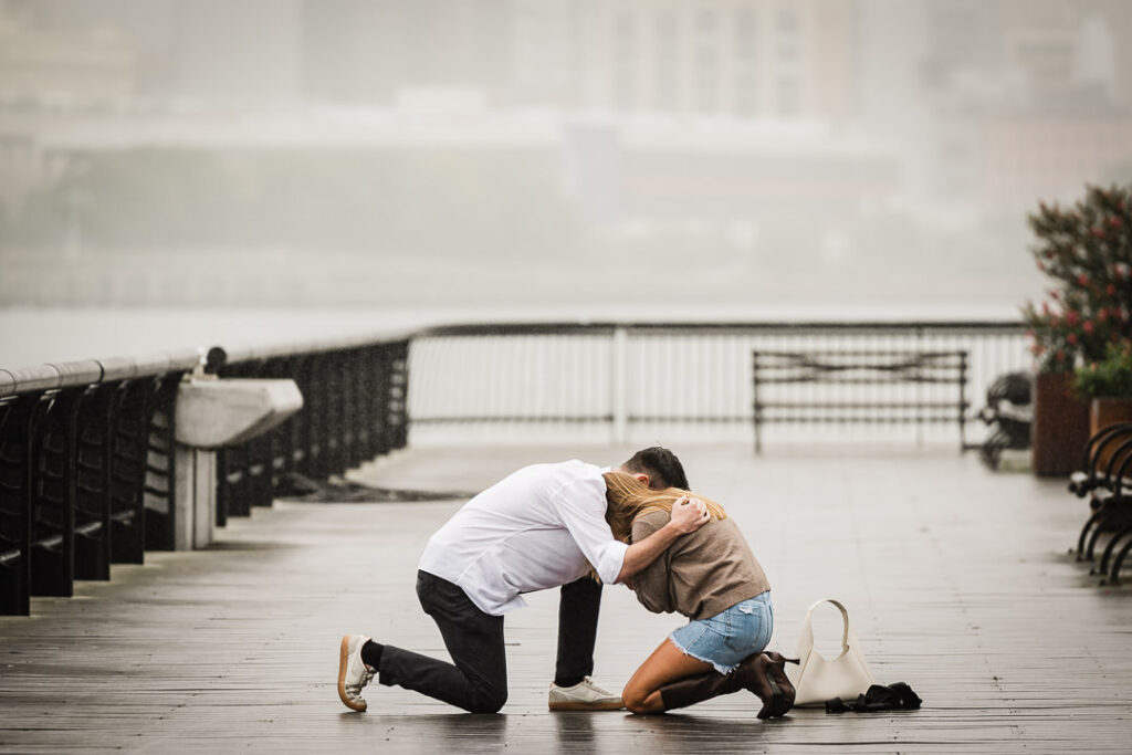 Engaged couple holding each other close after emotional proposal on rainy Pier 13 in Hoboken