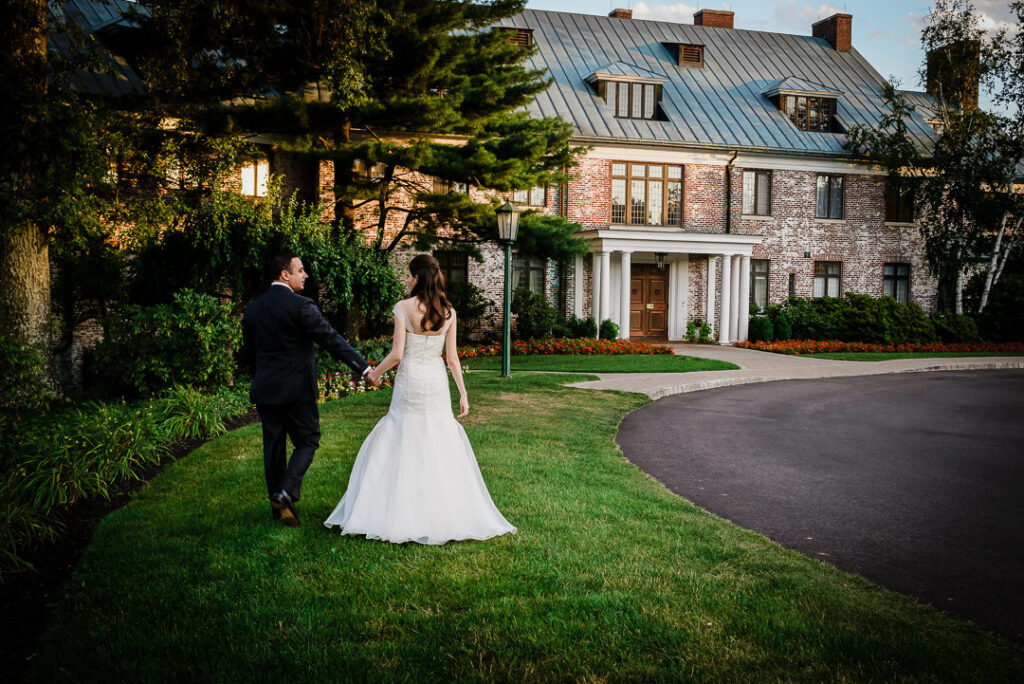 Newlyweds walking toward Hamilton Farm's illuminated copper roof building during magical blue hour