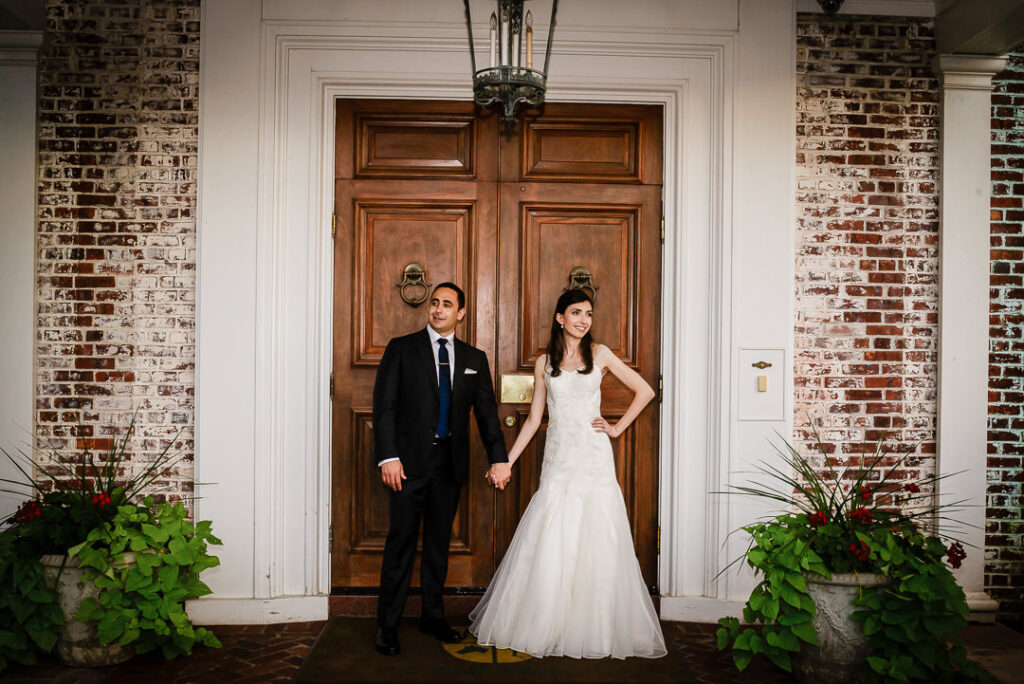 Elegant formal portrait of bride and groom standing before carved wooden doors with white architectural trim