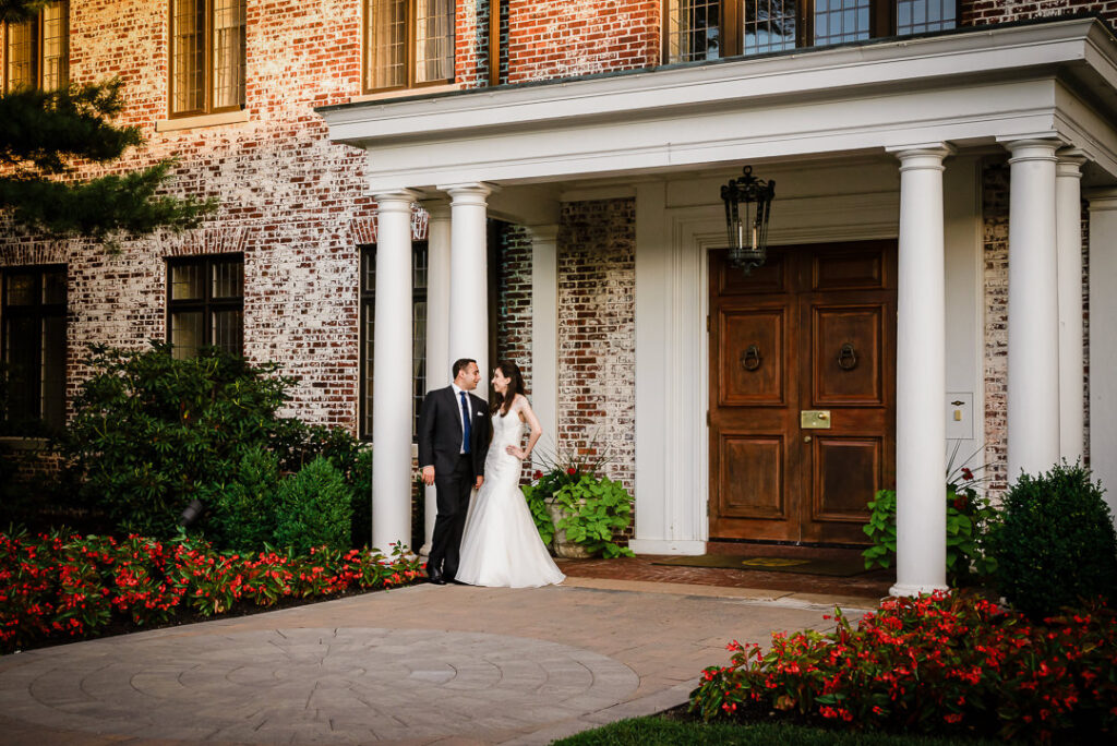 Newlyweds posing at Hamilton Farm's iconic entrance with towering white columns and exposed brick walls