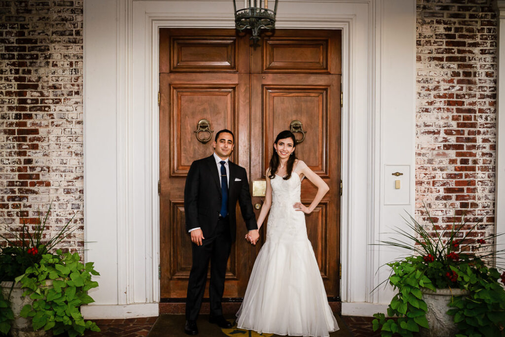Bride and groom holding hands in front of Hamilton Farm's stately entrance with lion door knockers