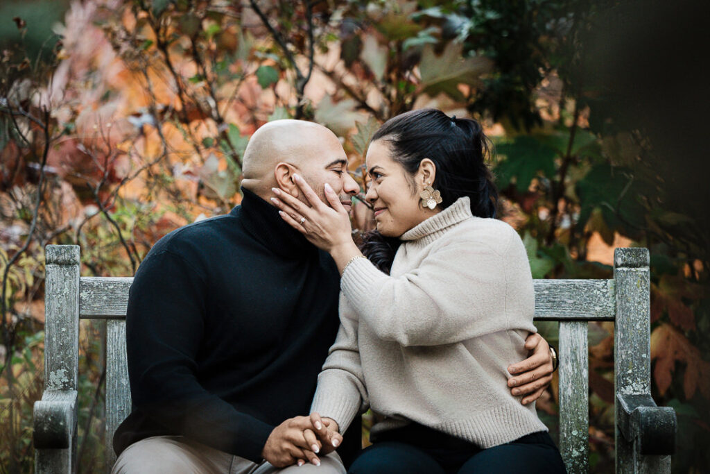 Engaged couple shares intimate moment on Van Vleck garden bench with autumn colors, Northern New Jersey engagement photographer
