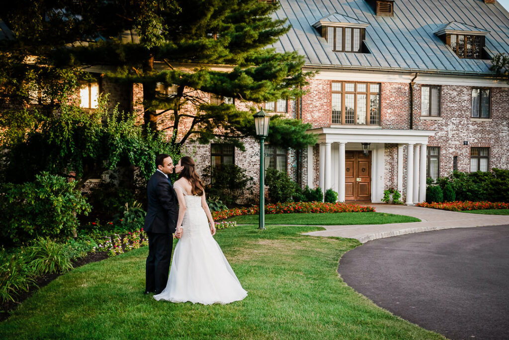 Romantic evening portrait of couple kissing with Hamilton Farm's architecturally lit brick building behind them