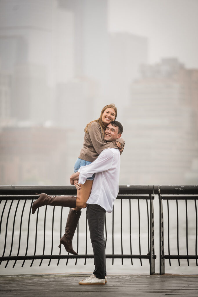 Playful newly engaged couple with bride on groom's back celebrating on Pier 13 boardwalk