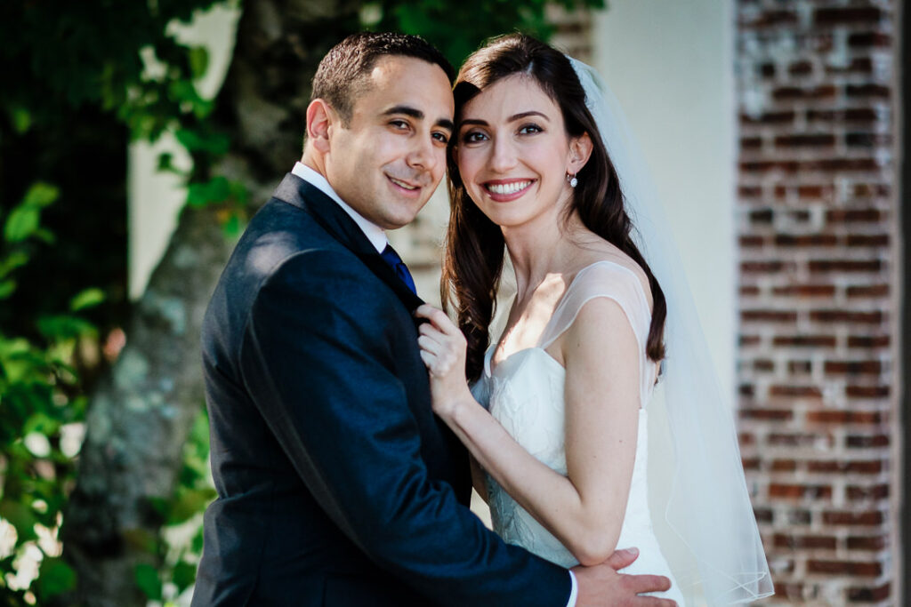 Jewish wedding couple embracing in sunlit garden with exposed brick at Hamilton Farm Golf Club