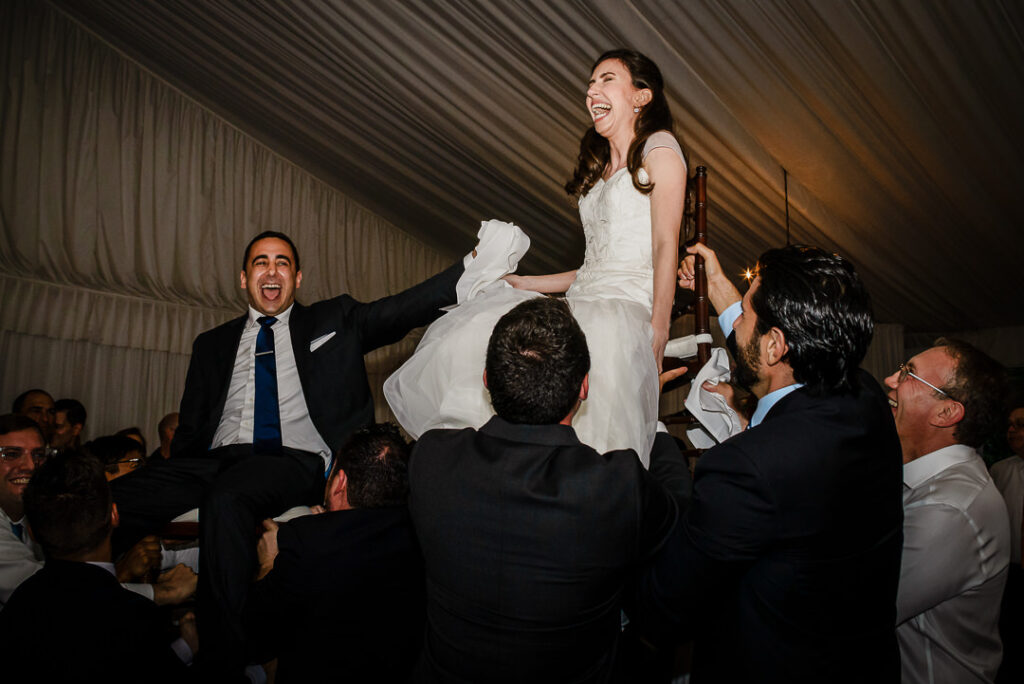 Ecstatic couple raised high on chairs with pure joy and laughter during Hora at Hamilton Farm reception