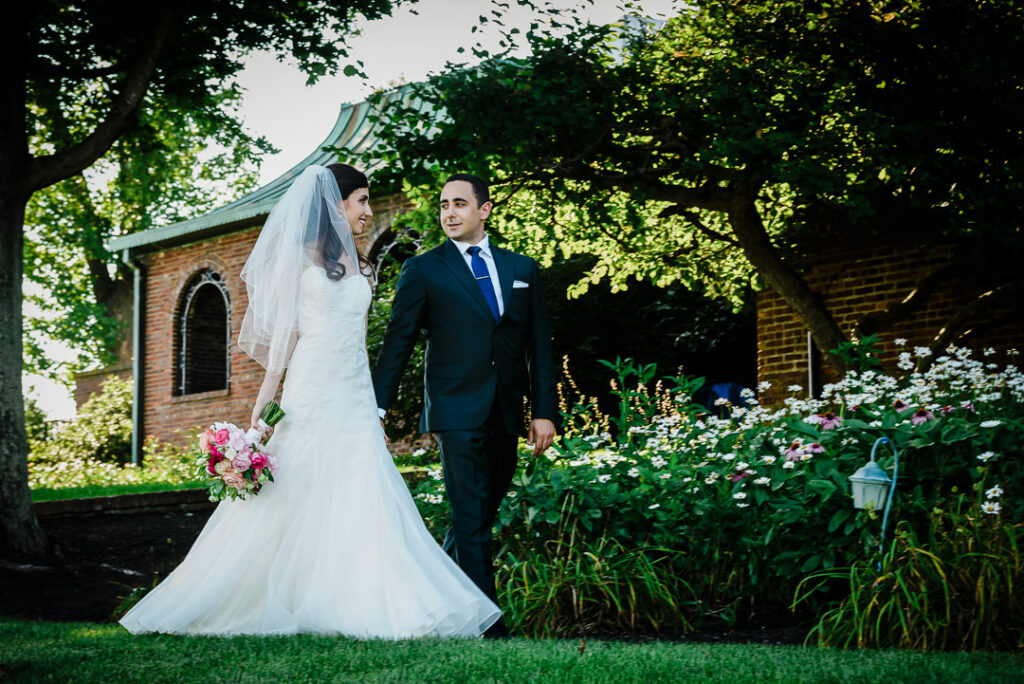 Newlyweds walking hand in hand past historic brick garden structure at Hamilton Farm Golf Club