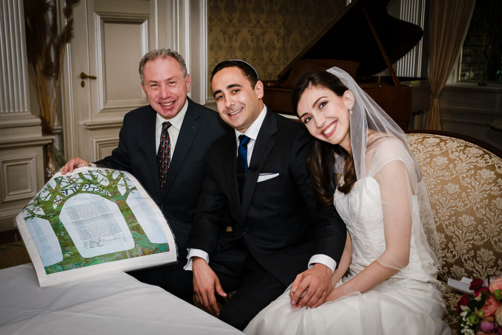 Happy couple with rabbi displaying signed Ketubah with decorative tree of life design