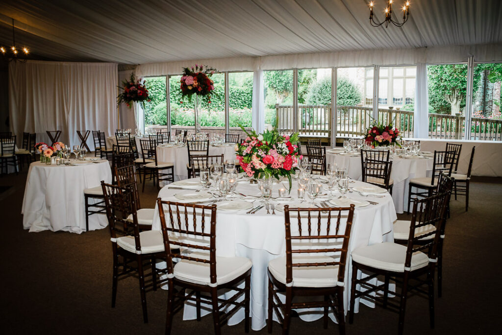 Sophisticated tented reception with white linens, mahogany chiavari chairs, and tall crimson floral centerpieces