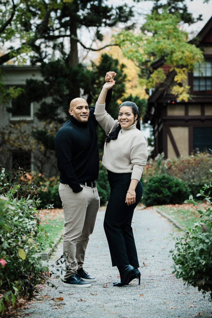 Newly engaged couple celebrates with raised hands on Van Vleck Gardens pathway, joyful fall engagement photos Montclair NJ