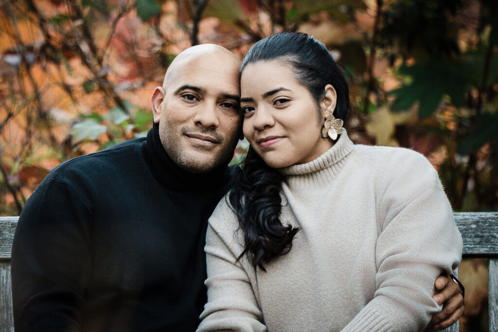 Engagement portrait of couple on weathered garden bench at Van Vleck with autumn foliage background, Alex Kaplan Photography Northern New Jersey