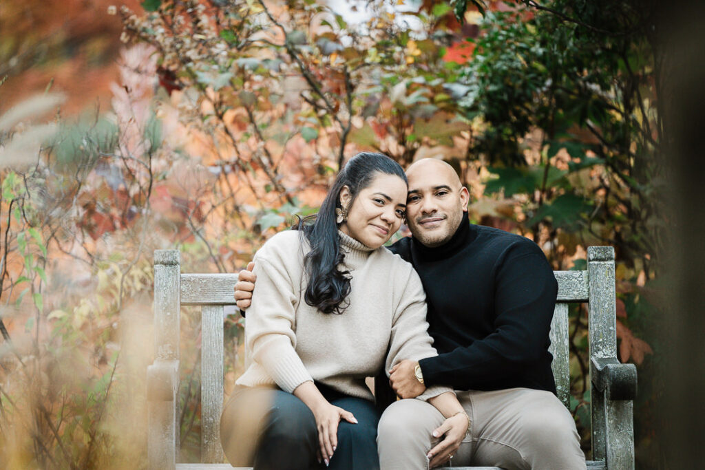 Romantic moment between newly engaged couple on Van Vleck garden bench surrounded by fall foliage, Northern New Jersey photographer