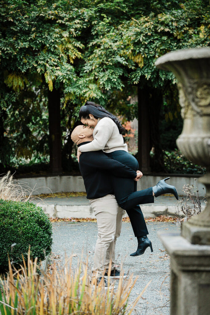 Engaged couple shares playful moment on Van Vleck Gardens path with autumn foliage backdrop, Alex Kaplan Photography Montclair NJ
