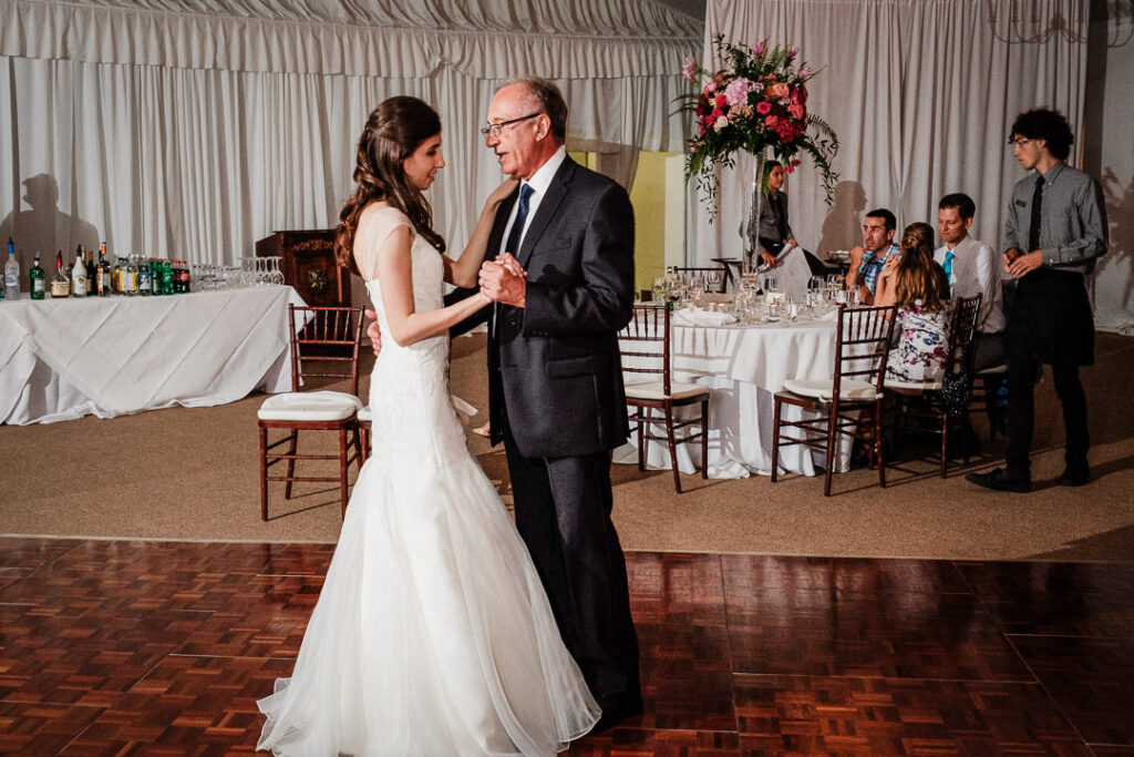 Father and daughter dancing together on parquet floor with full reception tent and guests in background