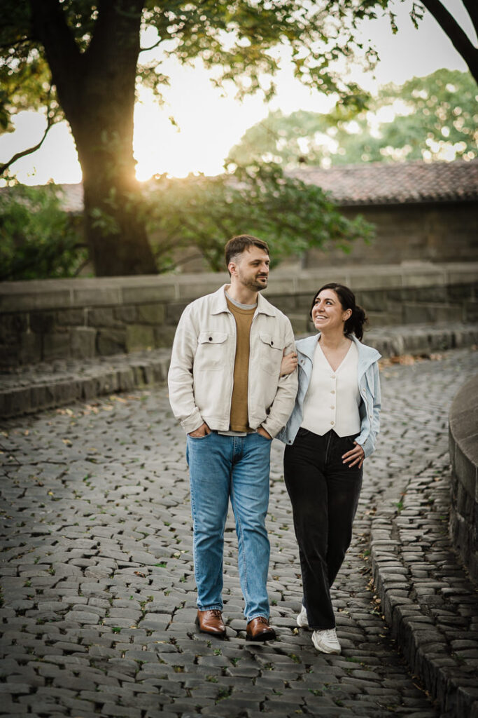 Golden hour engagement photo of couple walking at Fort Tryon Park with sunset lighting