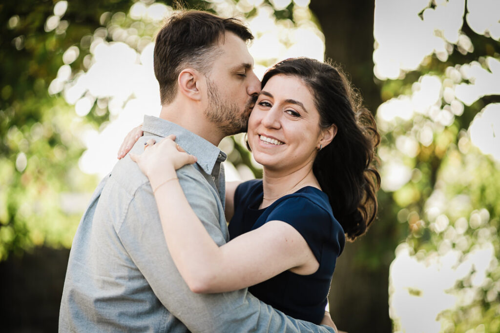 Romantic engagement photo of couple with kiss and natural bokeh at Fort Tryon Park NYC
