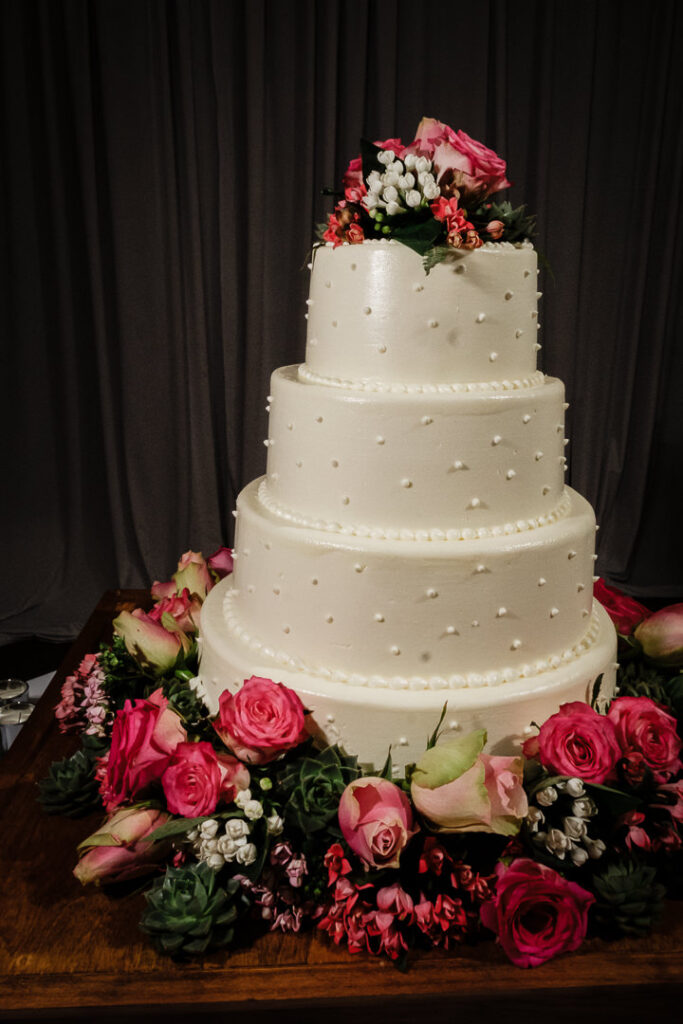 Stunning four-tier white wedding cake with pearl embellishments and cascading pink roses and succulents