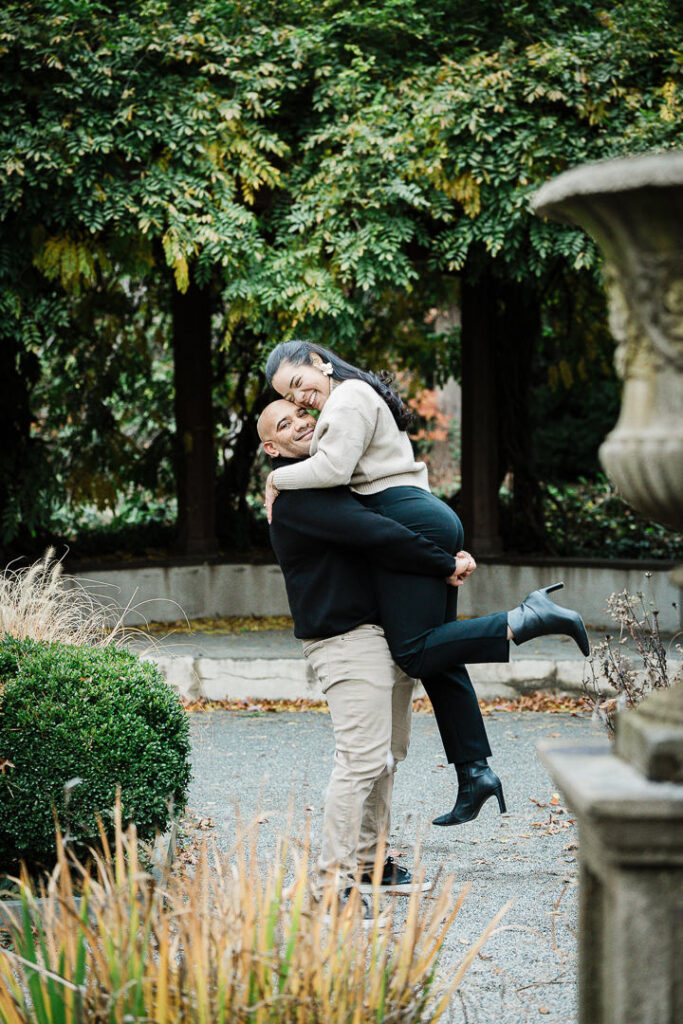 Groom lifts newly engaged bride on garden pathway at Van Vleck surrounded by fall foliage, Northern New Jersey engagement photographer
