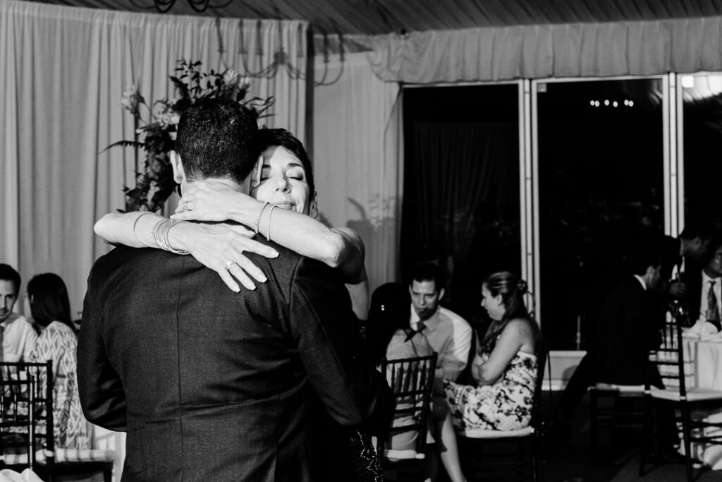 Touching black and white moment of groom embracing mother during special mother-son dance