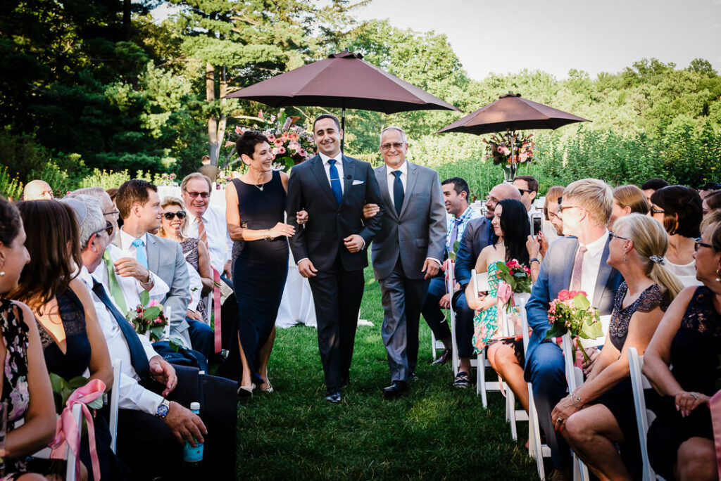 Groom walking down aisle escorted by both parents in Jewish wedding tradition at Hamilton Farm outdoor ceremony