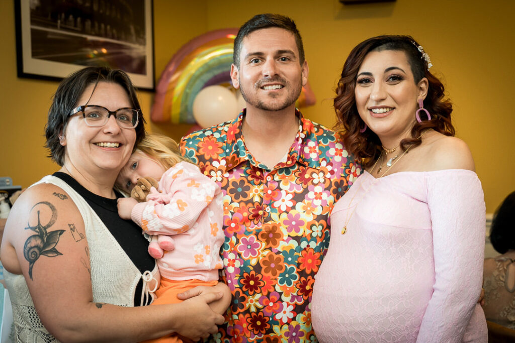 Family member holding baby at groovy themed baby shower with rainbow arch backdrop NJ