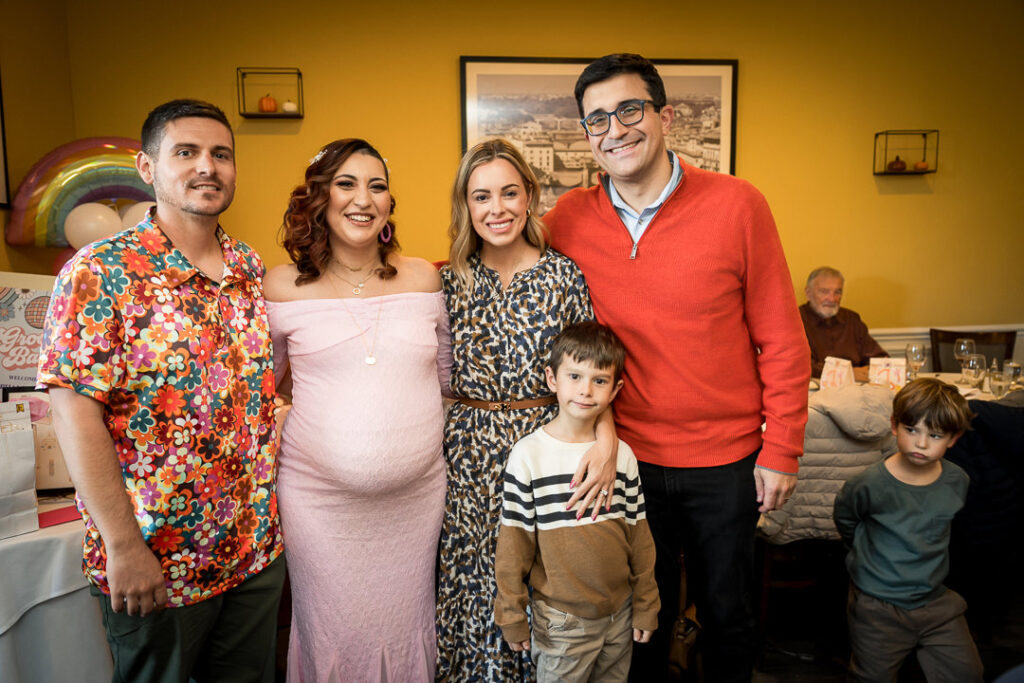 Three generations of family gathered beneath rainbow balloon arch at Delpino Restaurant baby shower