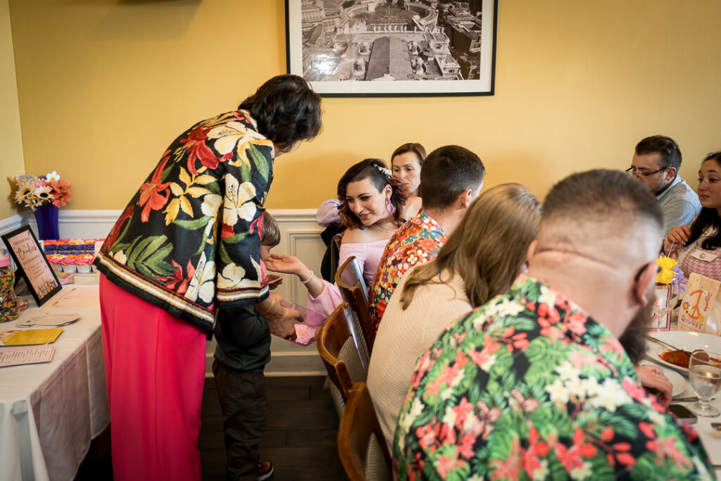 Mom-to-be opening baby gifts while guests watch at groovy themed baby shower Delpino NJ