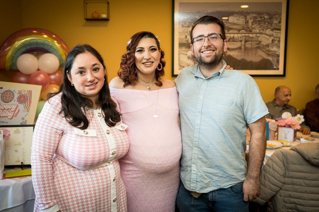 Siblings posing in front of rainbow balloon arch at groovy girl baby shower celebration