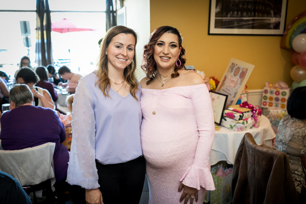 Friends posing by restaurant window with natural lighting at groovy baby shower Delpino NJ