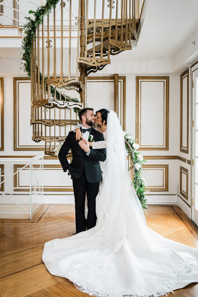 Bride and groom kissing on decorative spiral staircase at James Ward Mansion wedding photographed by Alex Kaplan