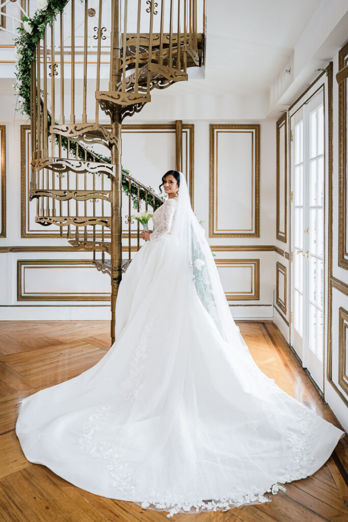 Bride in lace wedding gown with cathedral train poses on spiral staircase at James Ward Mansion wedding in Westfield NJ by Alex Kaplan Photography