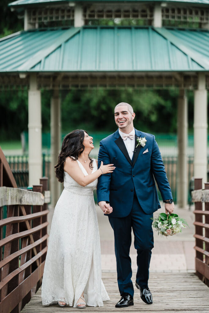 Bride and groom walking hand in hand laughing near gazebo in New Jersey wedding by Alex Kaplan Photography