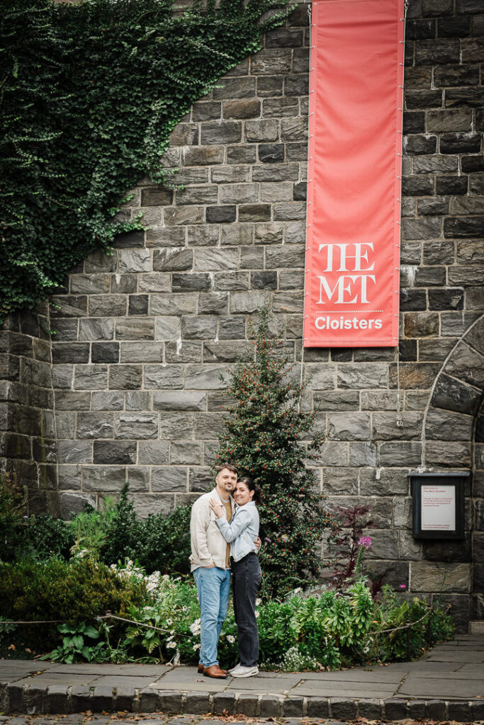Couple embracing at The Met Cloisters entrance with ivy-covered stone wall and museum banner