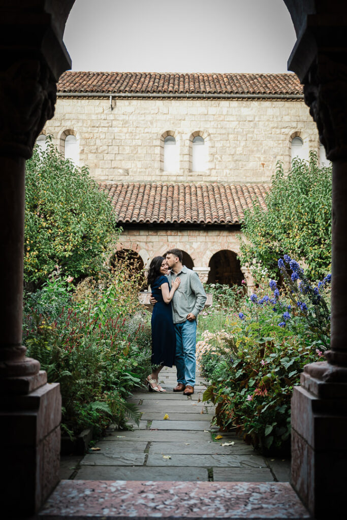 Couple portrait at historic courtyard featuring weathered stone arches and ornate columns with lush garden surroundings