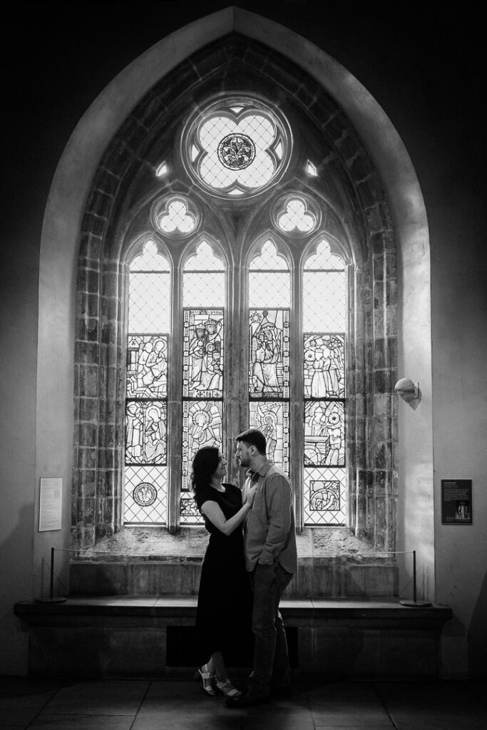 Black and white engagement photo of couple silhouetted against gothic stained glass window at The Met Cloisters