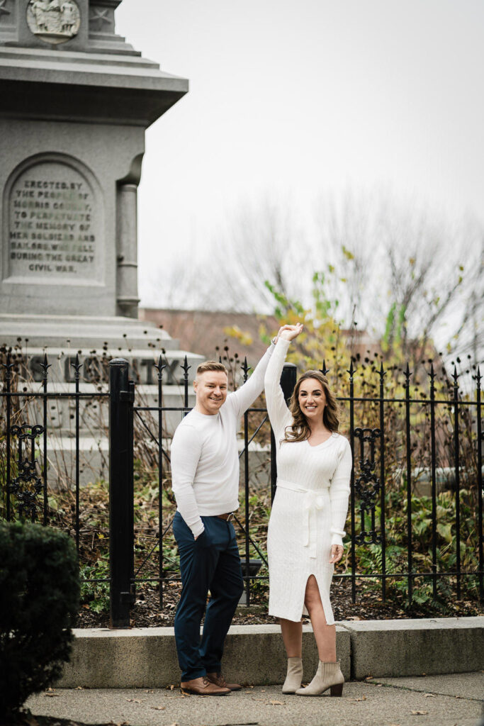  Engaged couple twirling and dancing at Morris County memorial in Morristown during fall engagement photo session