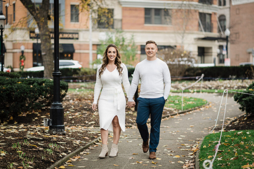 Candid engagement photo of couple walking through downtown Morristown in fall with autumn leaves and historic buildings