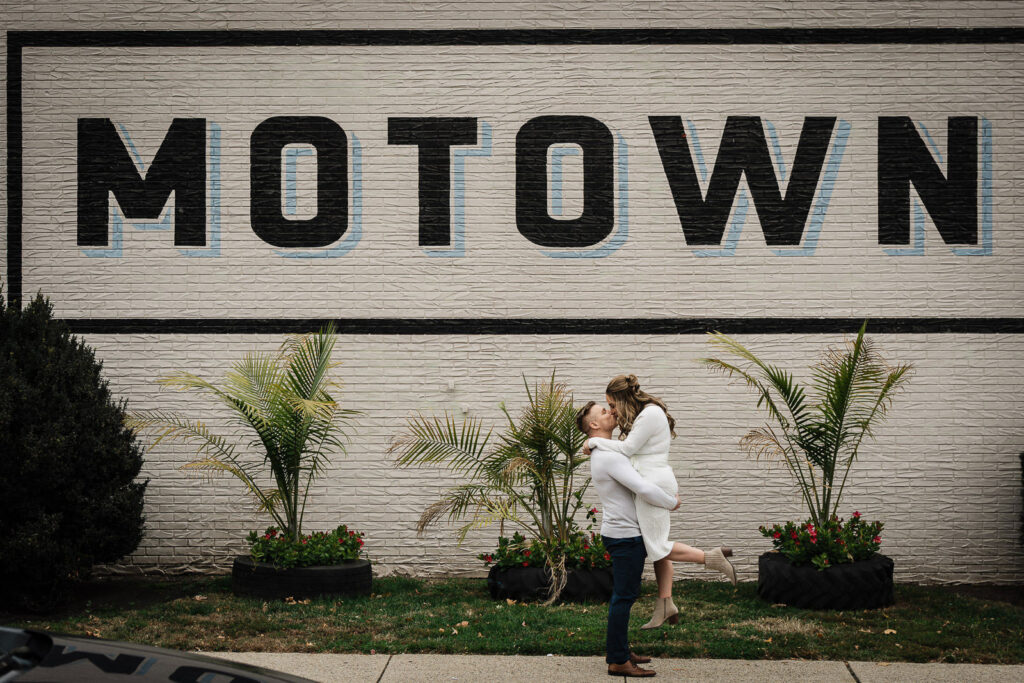 Groom lifting bride at MOTOWN mural during Morristown NJ engagement photo session with urban backdrop