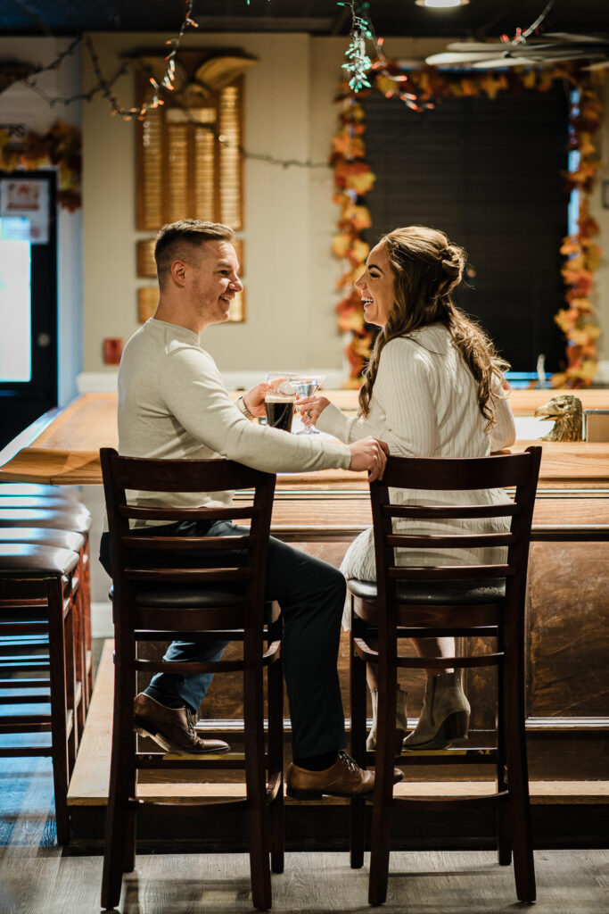 Engaged couple toasting Guinness and cocktail at local Morristown members bar during engagement photo session with autumn decor
