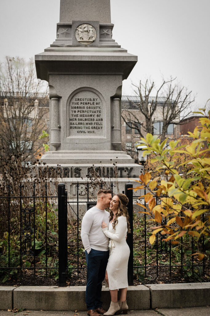 Engaged couple embracing at Morris County Civil War Memorial in Morristown New Jersey during fall engagement photography session