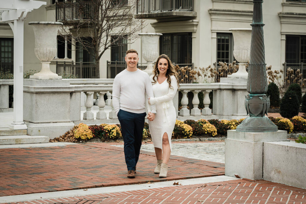 Engaged couple walking hand in hand at historic Morristown building with ornate fountain and colonial architecture
