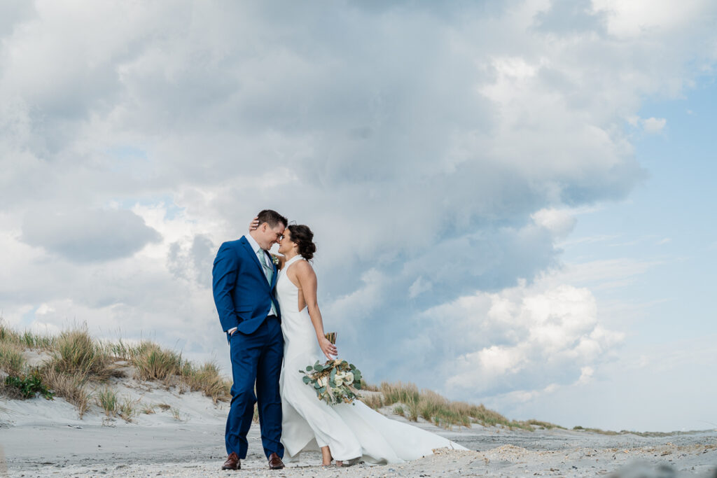 Romantic couple kissing on beach under dramatic cloudy sky during New Jersey wedding by Alex Kaplan Photography
